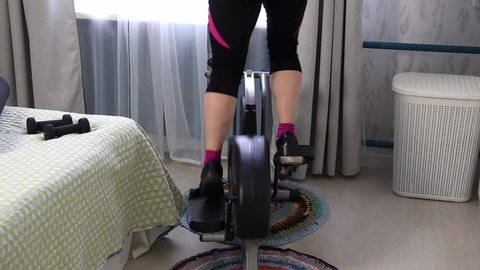 Overweight woman do workout with elliptical trainer at home during quarantine and look out the window. Time for self improvement concept.