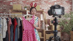 young charming asian japanese lady host celebrating christmas wearing reindeer antler and showing party dress to professional camera on tripod in live streaming online.
