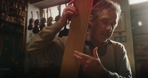 Cinematic shot of experienced master artisan luthier choosing fine quality wood for creation of handmade violin in creative workshop. Concept of spiritual instrument, art, orchestra, passion for music