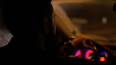 Close-up of a man with a beard drives a car at night against the background of burning lanterns