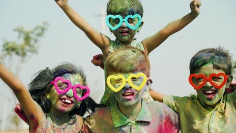 Group of Cheerful kids with fun spectacles Shouting at camera after playing with colourful holi powder during festival celebration