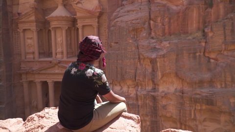 Man sitting and look into The Treasury ancient ruin building in Petra Jordan. Wide angle.
