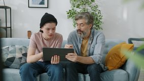 Father and teenage son are using tablet talking then doing high-five hand gesture spending leisure time at home. Fatherhood and modern technology concept. - Powered by Shutterstock - Get 15% off with code: PIKWIZARD15