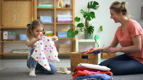 Mother and kid fold clothes, child girl help woman Spbd. Family do housekeeping chore together. Sort clean laundry in living room. Concept domestic, housewife, basket.