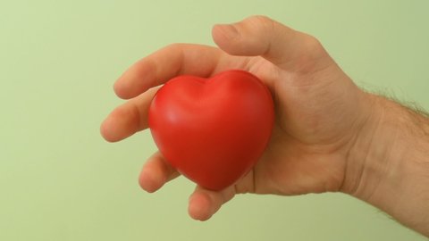 Young man's hand squeezes red anti-stress heart toy. Romantic love, calmness and peace, Saint Valentine's Day preparation design concept. Preparation for donation