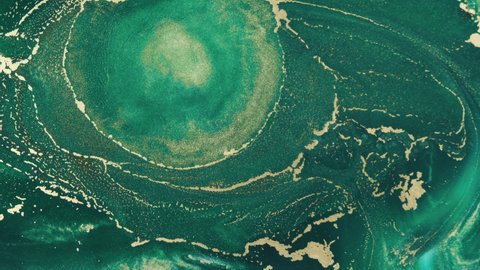 Abstract explosion of green paints gold sparkles close-up. Hypnotic current liquid ink. Emerald color of spreading, moving mesmerizing background. 4k footage. Texture of golden threads on green tide