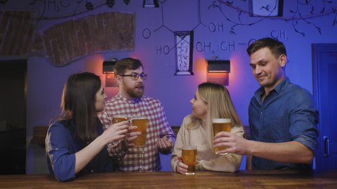 Friends in pub drink beer on bar counter clink glasses. Happy people enjoy weekend