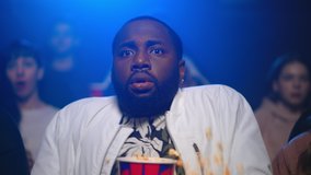 Shocked african american man watching scary film in movie theater. Portrait of bearded afro guy jumping in seat. Frightened afro american male person sprinkling popcorn in dark cinema. - Powered by Shutterstock - Get 15% off with code: PIKWIZARD15