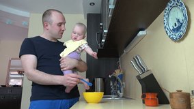 Loving father feed his baby son feed with spoon holding in hands in kitchen at home. Infant boy eating food mash. Static shot. 4K UHD video clip.