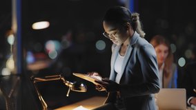 Young African American Female Boss Leaning on Corporate Table Desk Using Tablet Computer for Digital Management. Businessperson. Night Office. - Powered by Shutterstock - Get 15% off with code: PIKWIZARD15