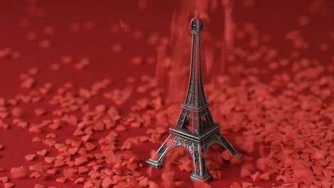 Eiffel tower statuette on red background red scarlet heart shaped sugar confetti fall down scatter slow motion. France, romantic love, Saint Valentine's Day preparation design concept