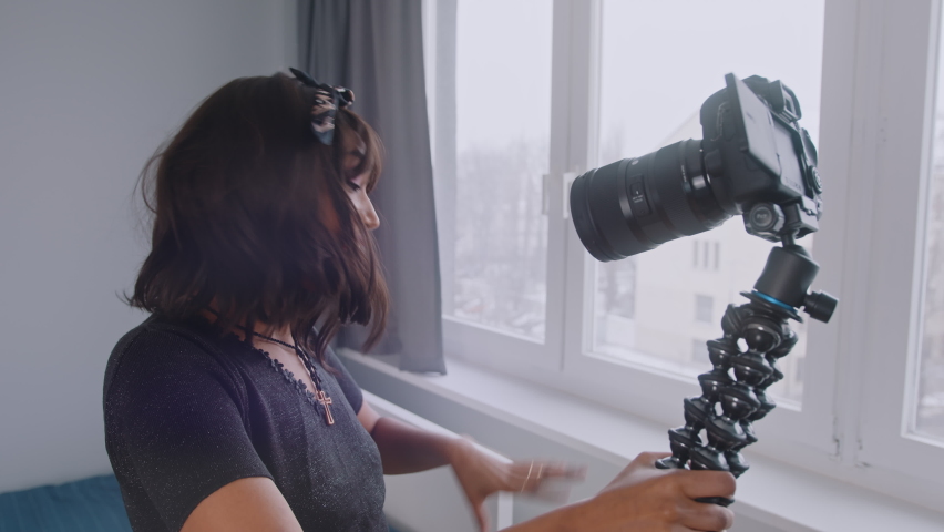 Cheerful young African American female blogger holding camera and recording video for vlog while standing near the window. High quality 4k footage