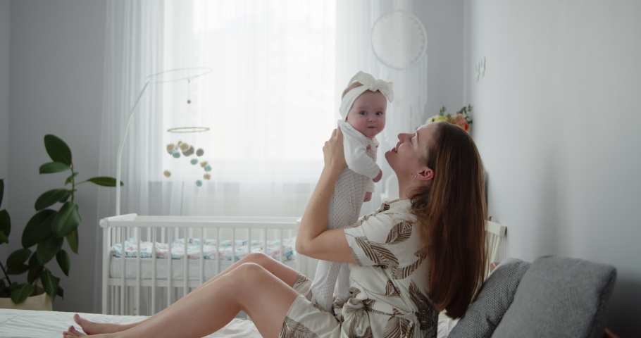 Young beautiful mother plays with her cute newborn baby that is sitting on mom