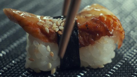 Sticks taking sushi from table, Closeup of eating tasty sushi rolls filled with eel. Sushi restaurant, food delivery. 