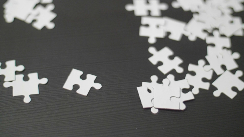 Close up of white blank puzzle pieces lying on a dark table with young men's hands taking pieces and trying to solve it. Shot from above with smooth dolly forward movement. Shot in 4K Slow Motion. | Shutterstock HD Video #1066747441