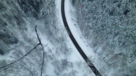 Aerial flight over cars driving along curvy rural road through snowy winter forest