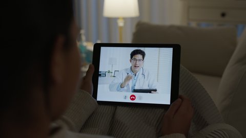 Over shoulder view of young asia woman talk to doctor on cellphone videocall conference medical app in telehealth telemedicine online service hospital quarantine social distance late night concept.