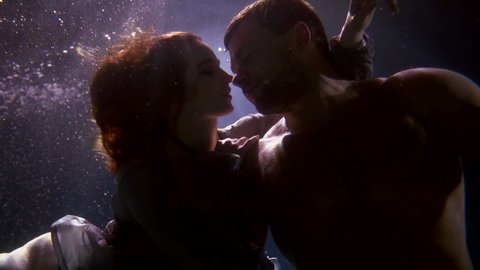 young redhead woman is seducing her brawny boyfriend underwater, two lovers are floating in depth of pool