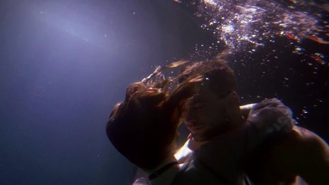 young heterosexual pair is floating underwater, romantic man and woman are hugging inside water