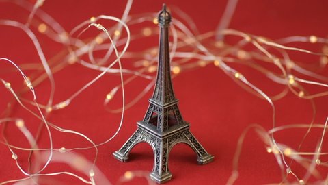 Eiffel tower statuette red lights garland background scarlet heart shaped sugar confetti fall down scatter. France, romantic love, Valentine's Day preparation design concept
