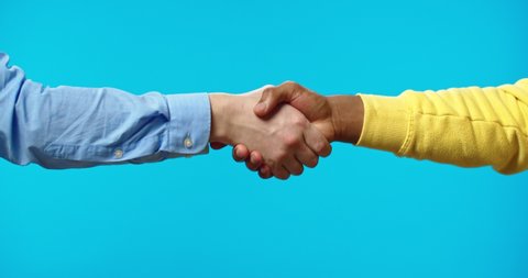 Close up shot of African American person hand shaking Caucasian hand isolated on blue background in studio, mixed-races men shake hands on blue wall, hand gesture, deal, business concept