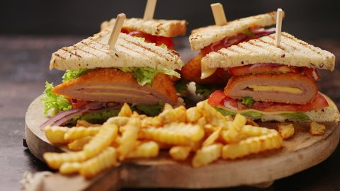 Club sandwiches served on a wooden board. With hot French fries