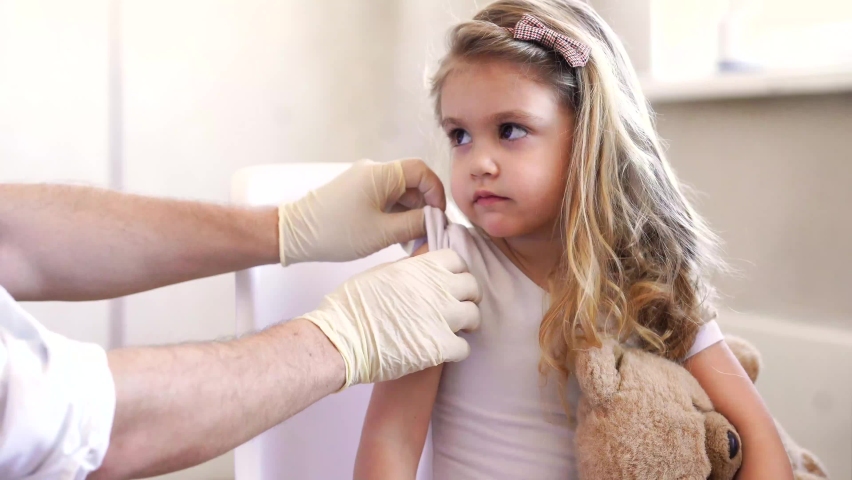 Immunization for children concept. Happy little cute blonde girl holding a toy and getting a flu shot not afraid of the syringe needle. Doctor injecting brave child with Covid-19 vaccine at clinic or Royalty-Free Stock Footage #1066768465