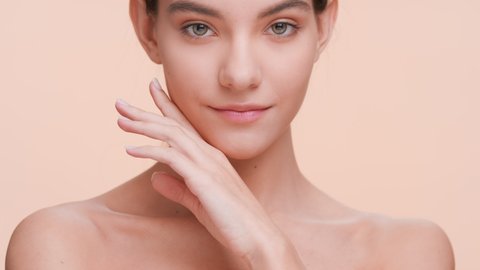 Close up beauty portrait of young good-looking woman who softly touches her chin with a back of her hand, gently lays fingers on the jowl and smiles | Perfect skin and beauty care concept