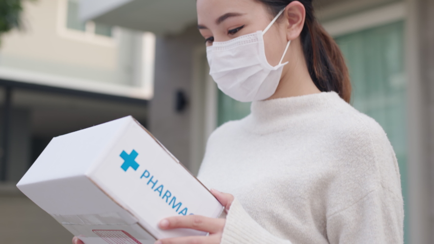 Young attractive beautiful asian female receive medication package box free first aid from pharmacy hospital delivery service at home wear glove, face mask in telehealth, telemedicine online concept. | Shutterstock HD Video #1066779472