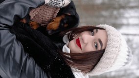 Young girl holds her dachshund dog in the winter park. Vertical video