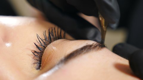 Beautician in black gloves making permanent makeup correction eyebrows shape. Microblading, eyebrow tattoo in beauty salon. Female master using special needle, injects pigment into skin. 4 k video