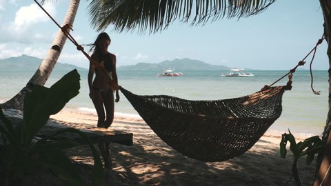 Slow motion woman going beach on El Nido island, Philippines, Asia. Traditional boat on tropical turquoise ocean water. Sunbed with hammok under palm trees. Cinematic footage shot in 4K
