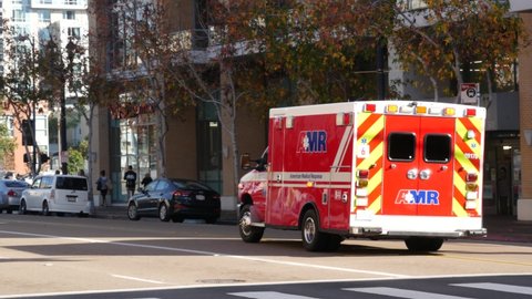 San Diego, California USA - 4 Jan 2020: AMR american medical response ambulance car. EMS emergency service red vehicle, downtown city street. Paramedic rescue truck. 911 public safety. Man on scooter.