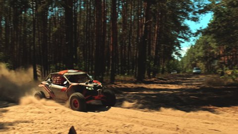 Cinematic clip of a buggy car going in cross country road. Fast buggy is driving with big clouds of dust. Speed riding of a racing off-road car in the forest road. 