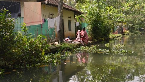 Alleppey, India - January, 29, 2016: Swimming on tourist boat on beautiful canals and lagoons of Kerala. View on a village from water, woman washing clothes in river, Kerala, Alappuzha backwaters