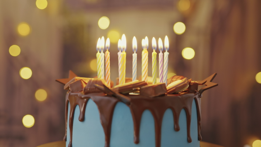 Birthday Cake with Burning Candles is Rotating on Stand on Table in House. Bright Dessert for a Child's Birthday Party on Background of Bokeh Light Bulbs Garlands. Family Holiday. Childhood | Shutterstock HD Video #1066800157