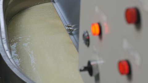 Milk cheese mass is stirred in a large tank with special whisks. Cheese production in a small family-run cheese factory. Buttons and lights on the control unit light up