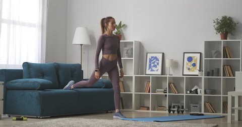 woman is squatting in living room of modern apartment, training and doing physical exercise for health and beauty, full lenght