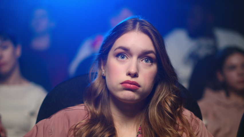 Closeup young woman feeling angry with bad film indoors. Portrait of disappointed girl looking smartphone on movie in cinema. Shocked lady holding cellphone in movie theater. | Shutterstock HD Video #1066809892