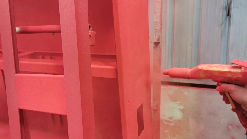 Painter spraying red powder coating on metal cabinet.