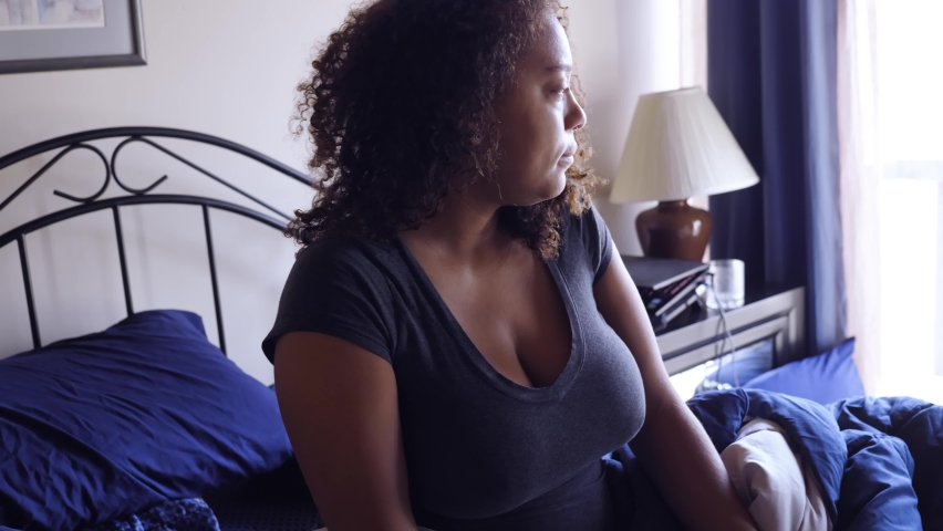 Portrait of a mixed race black woman with curly afro hair is sitting in the bedroom with a cup of coffee. the natural window light touches the skin gently while she enjoys her vacation.  | Shutterstock HD Video #1066813672