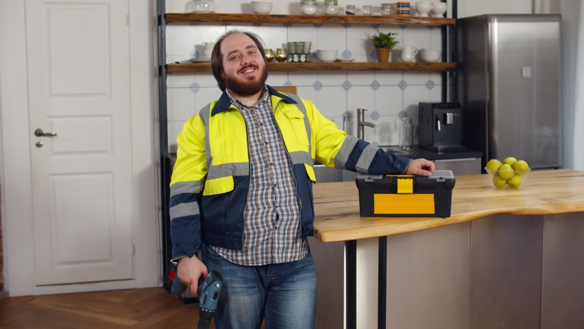 Portrait of funny male worker in uniform with screwdriver in kitchen. Overweight handyman holding electric drill and smiling at camera standing in modern kitchen with toolbox Royalty-Free Stock Footage #1066813906
