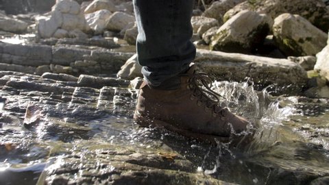 Close-Up Traveler Man Walks Along the River to Mountains. Hike in Boots Go Steps Stone Road on Background a Beautiful Landscape. Travel Concept Active People on the One Way to Move Forward Slow Motion