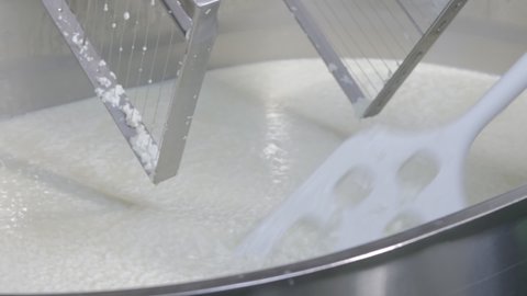 The cheese maker mixes the cheese mass in a stainless steel tank by hand with a perforated plastic mixer. The cheese making process in a private cheese factory