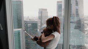 Modern teenage girl taking a selfie with her favorite toy near the window in a modern apartment overlooking the city from a high floor. Technology concept, new generation of youth
