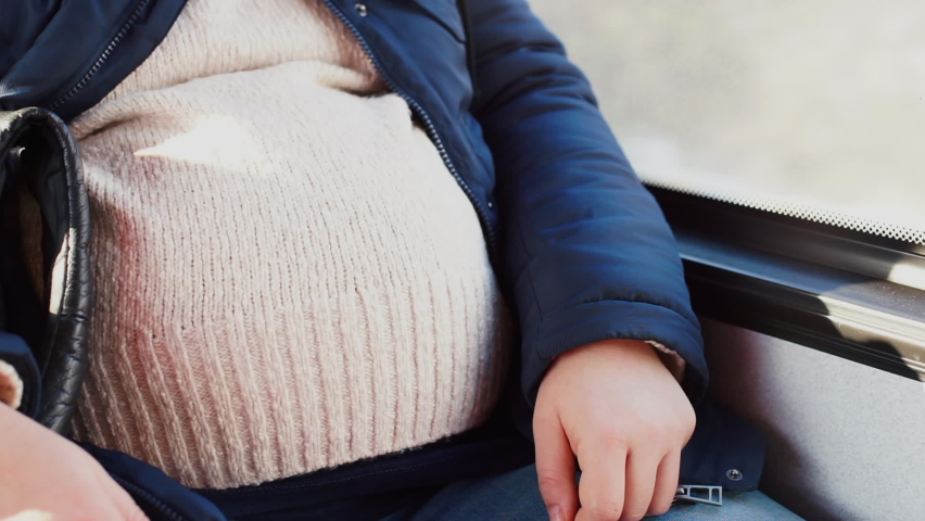 Belly pregnant woman on bus. She goes to prenatal clinic to managing pregnancy complications. Transportation passengers along the route in city. Addressing maternal concerns and questions. Close up. Royalty-Free Stock Footage #1066827466