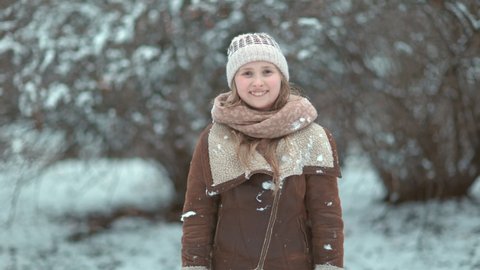 Portrait of smiling stylish child outside in the city park in winter in a knitted hat and sheepskin coat.