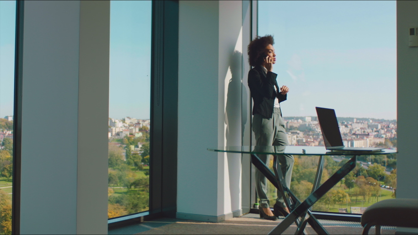 A young businesswoman talking on her mobile phone while standing near office window with a beautiful view.