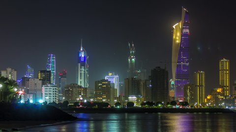 KUWAIT - CIRCA FEB 2019: Skyline with Skyscrapers night timelapse in Kuwait City downtown illuminated at dusk. View from beach with reflection in water. Kuwait City, Middle East.