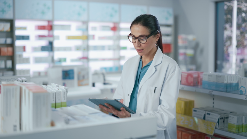 Pharmacy Drugstore: Beautiful Caucasian Pharmacist Uses Digital Tablet Computer, Checks Inventory of Medicine, Drugs, Vitamins, Health Care Products on a Shelf. Professional Pharmacist in Pharma Store Royalty-Free Stock Footage #1066836058